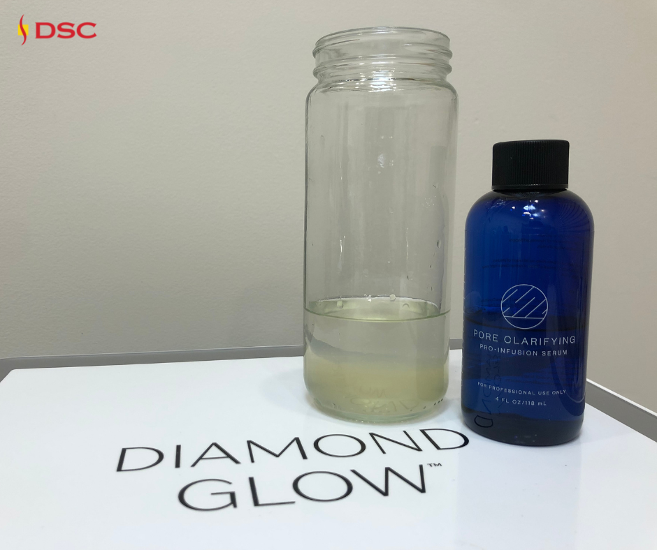 DiamondGlow waste water jar with dirt, oil and dead skin in used serum in a jar on top of DiamondGlow device beside a bottle of the Pore Clarifying SkinMedica Pro Infusion Serum