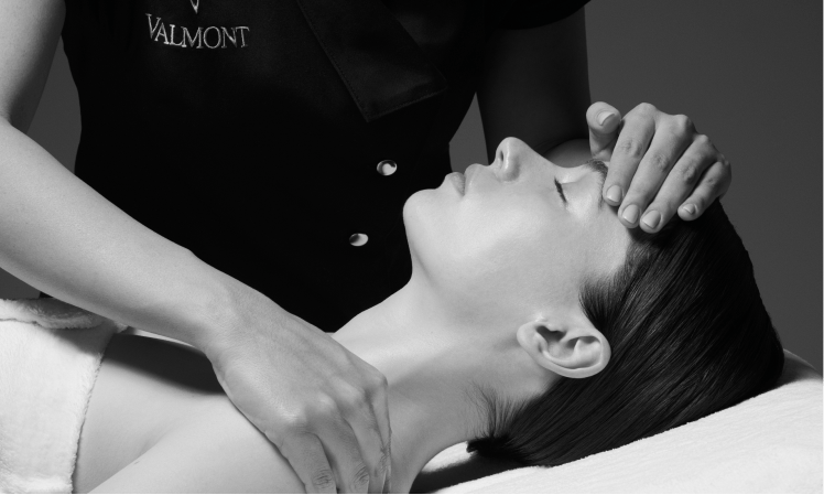 valmont facial with aesthetician hands resting on forehead and shoulder of client